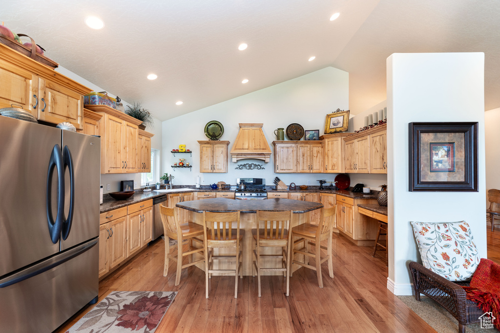 Kitchen with stainless steel appliances, a kitchen island, vaulted ceiling, a breakfast bar, and premium range hood