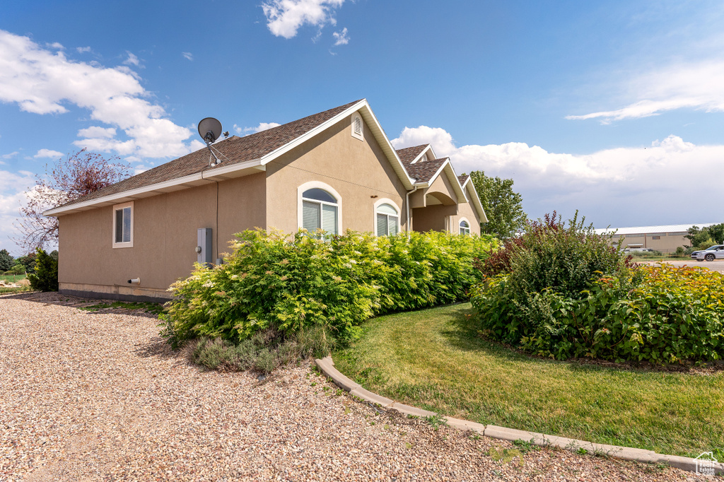 View of property exterior featuring stucco siding, a shingled roof, and a yard