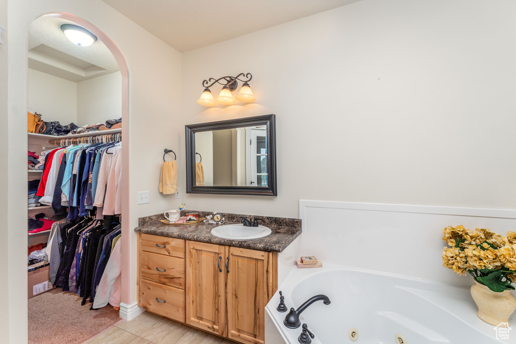 Bathroom with vanity, a tub with jets, and a walk in closet