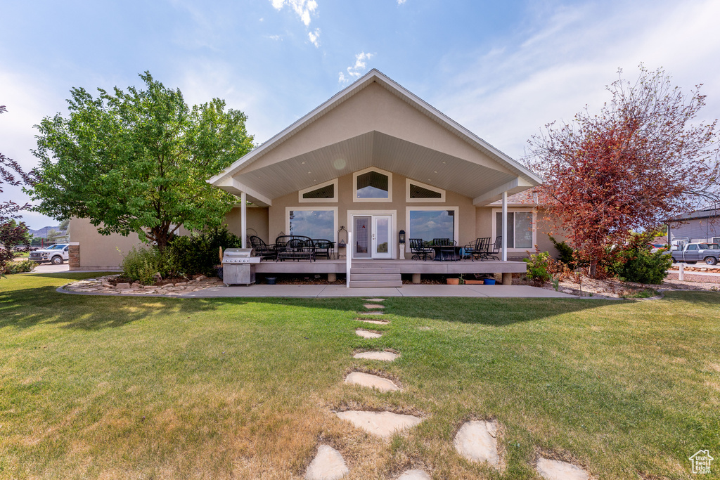 Back of property featuring a deck, a lawn, stucco siding, and french doors