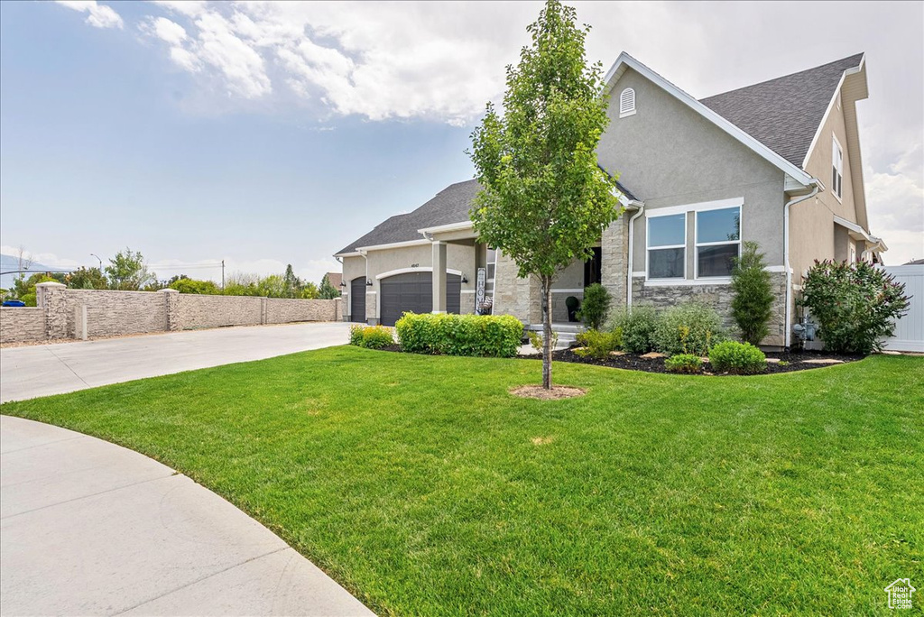 View of front of house with concrete driveway, stone siding, a front yard, a garage, and stucco siding
