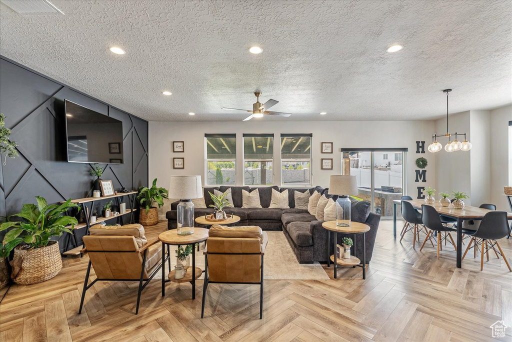 Living room featuring a textured ceiling, a ceiling fan, a chandelier, and recessed lighting