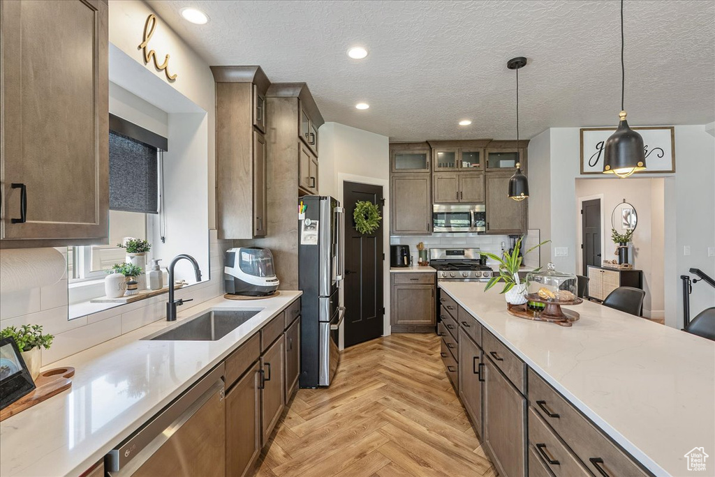 Kitchen with stainless steel appliances, glass insert cabinets, hanging light fixtures, a textured ceiling, and recessed lighting