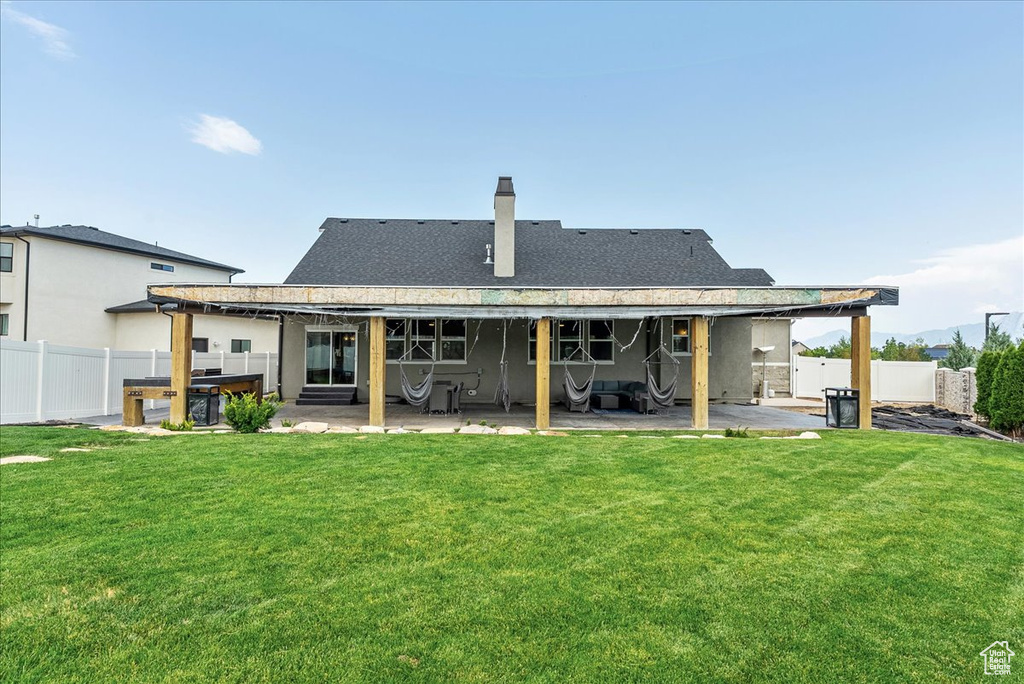 Back of property featuring a patio, a chimney, a shingled roof, and a hot tub