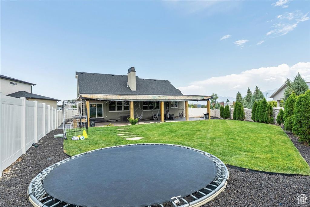 Rear view of house with a patio area, a chimney, a trampoline, a fenced backyard, and roof with shingles
