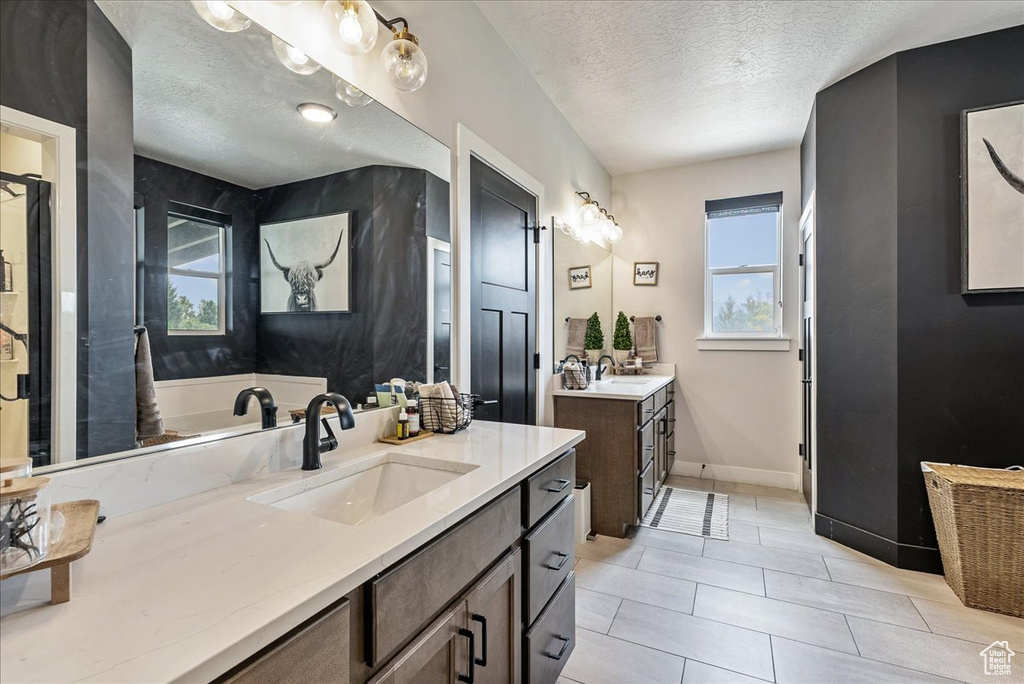 Full bath featuring a textured ceiling, healthy amount of natural light, two vanities, and tile patterned flooring