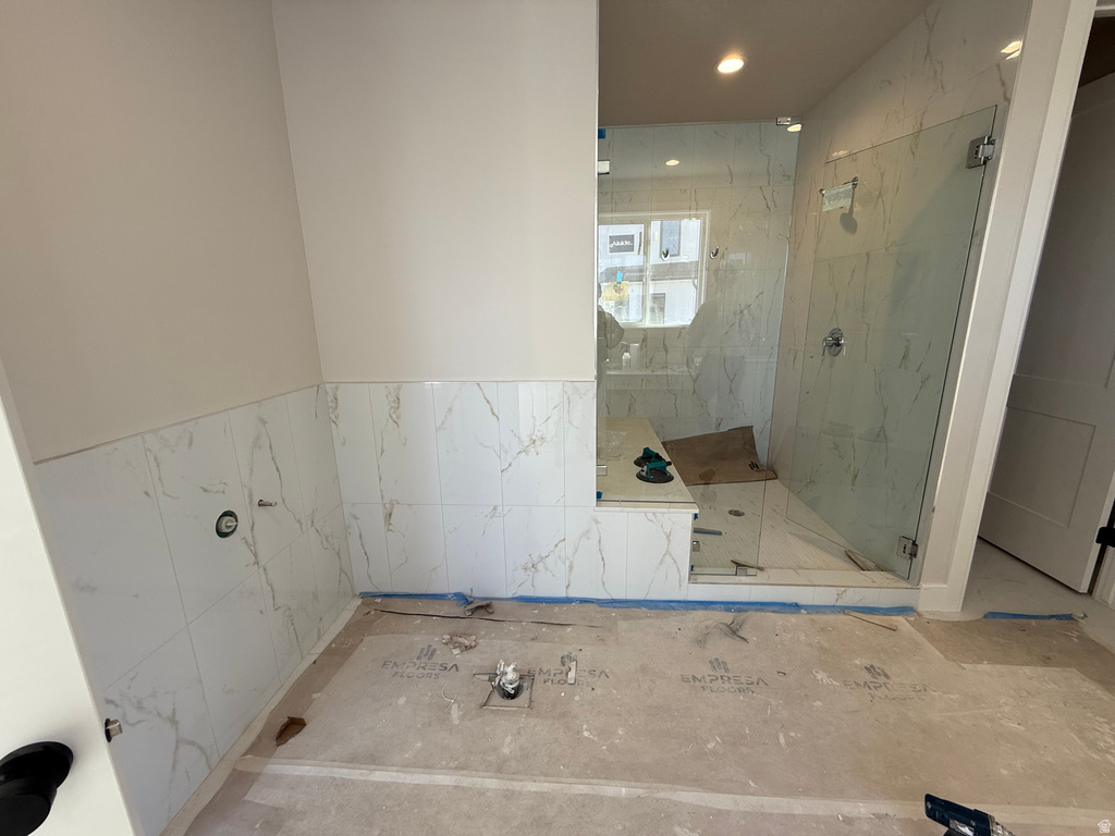 Full bath with a marble finish shower, tile walls, recessed lighting, and a wainscoted wall