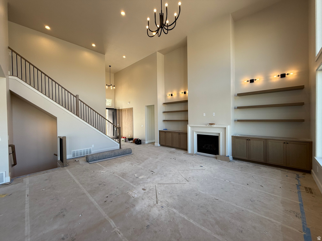Unfurnished living room with a towering ceiling, a chandelier, a fireplace, and recessed lighting