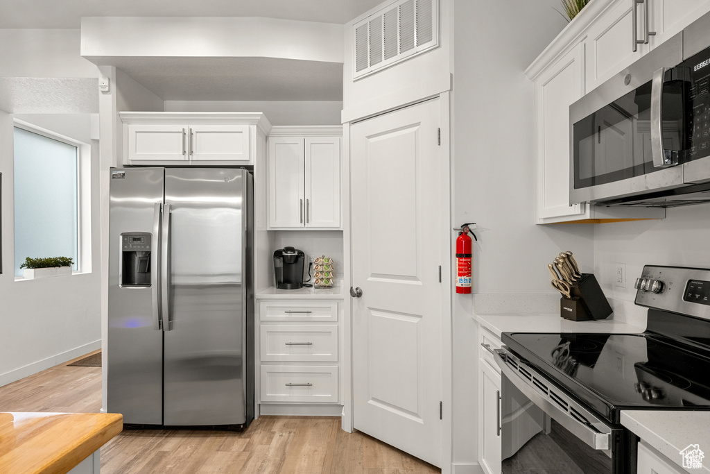 Kitchen featuring appliances with stainless steel finishes, white cabinets, and light wood-style floors