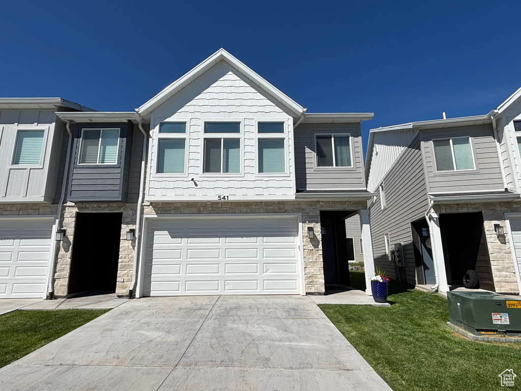 Traditional home featuring stone siding, driveway, an attached garage, and a front lawn