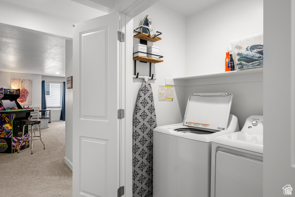 Laundry area featuring light carpet, washing machine and dryer, and a textured ceiling