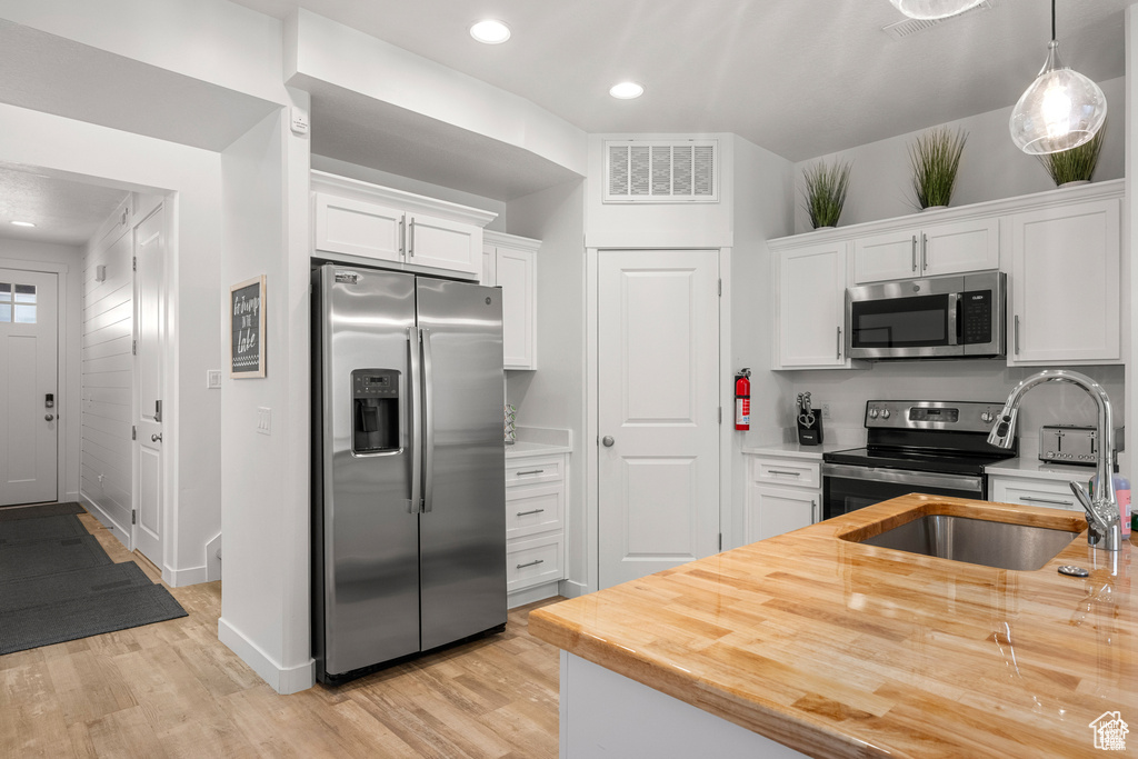 Kitchen with appliances with stainless steel finishes, white cabinetry, recessed lighting, pendant lighting, and light wood finished floors