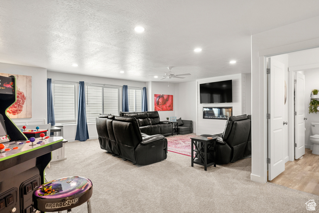 Living area with light carpet, a ceiling fan, a textured ceiling, recessed lighting, and a glass covered fireplace