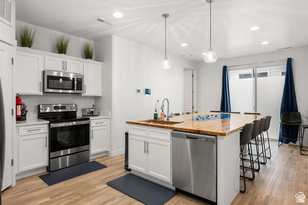 Kitchen featuring stainless steel appliances, white cabinets, an island with sink, light wood-style flooring, and recessed lighting