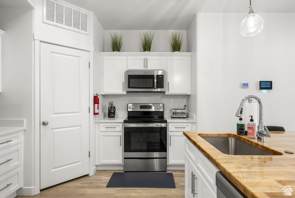 Kitchen with white cabinets, hanging light fixtures, appliances with stainless steel finishes, light wood-style flooring, and light stone counters