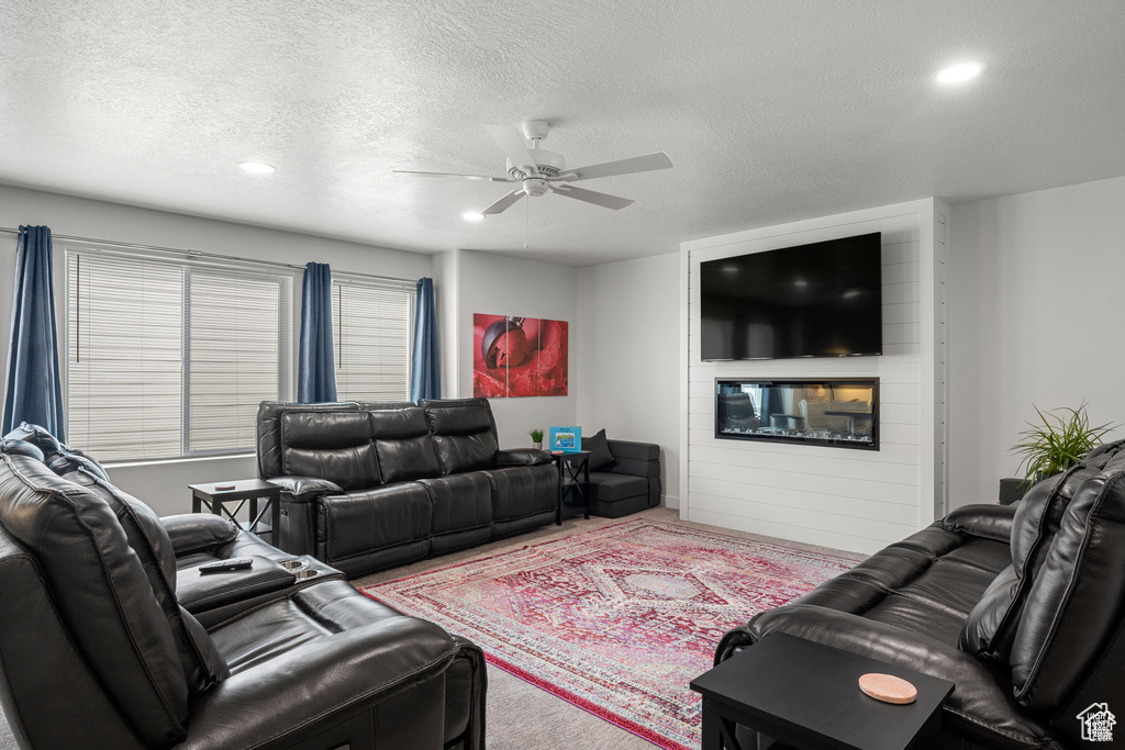 Living area with a textured ceiling, recessed lighting, ceiling fan, carpet flooring, and a large fireplace