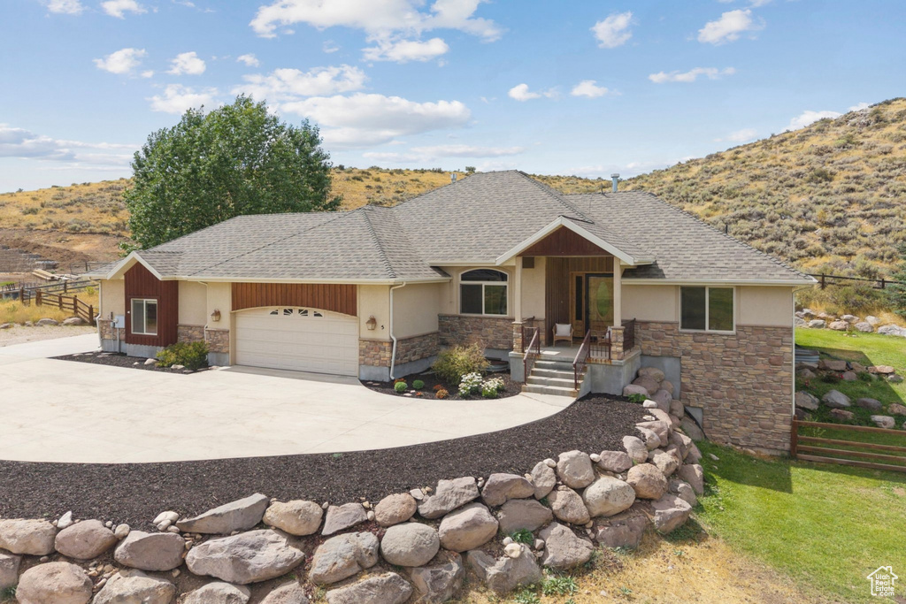 View of front of property with an attached garage, driveway, stone siding, covered porch, and a shingled roof