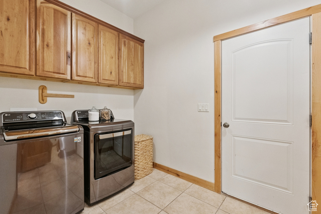 Laundry area featuring light tile patterned floors, separate washer and dryer, and cabinet space