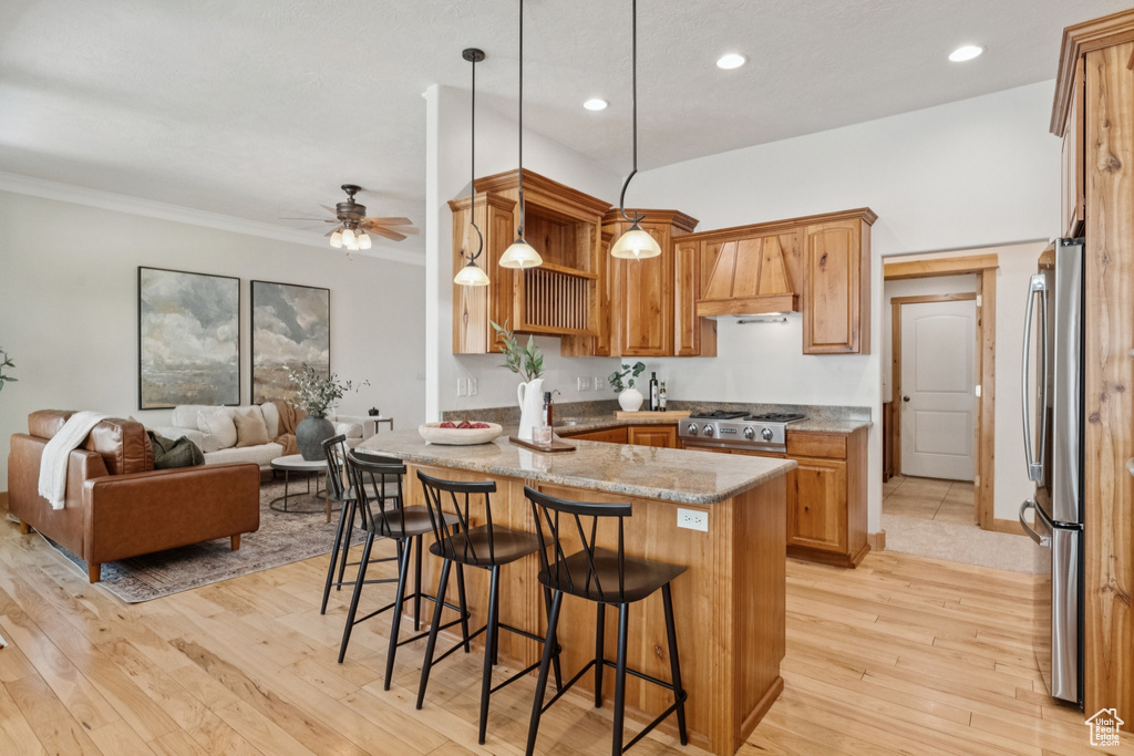 Kitchen with a peninsula, light stone counters, hanging light fixtures, light wood-style floors, and premium range hood