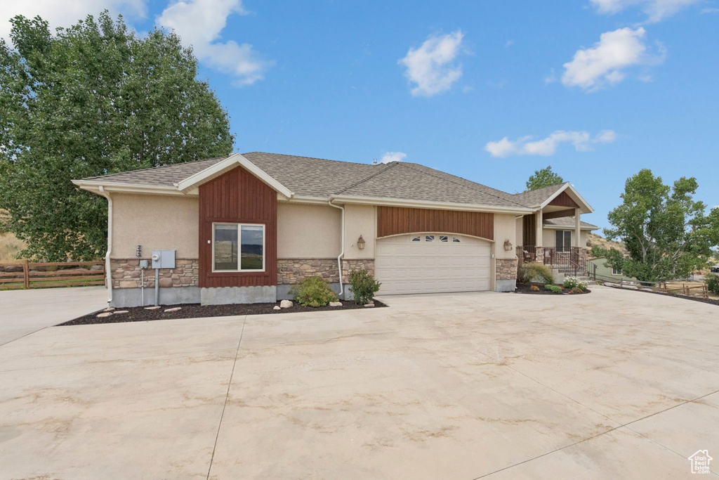 View of front facade featuring a garage, driveway, stone siding, a shingled roof, and stucco siding