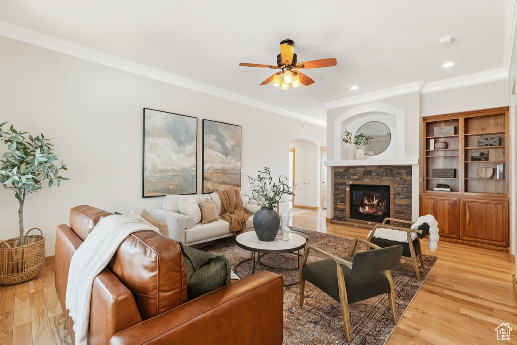 Living area with arched walkways, light wood-style floors, ornamental molding, a stone fireplace, and recessed lighting