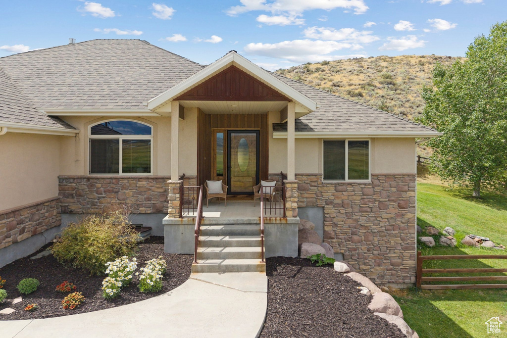 Property entrance with stone siding, a shingled roof, stucco siding, and a porch