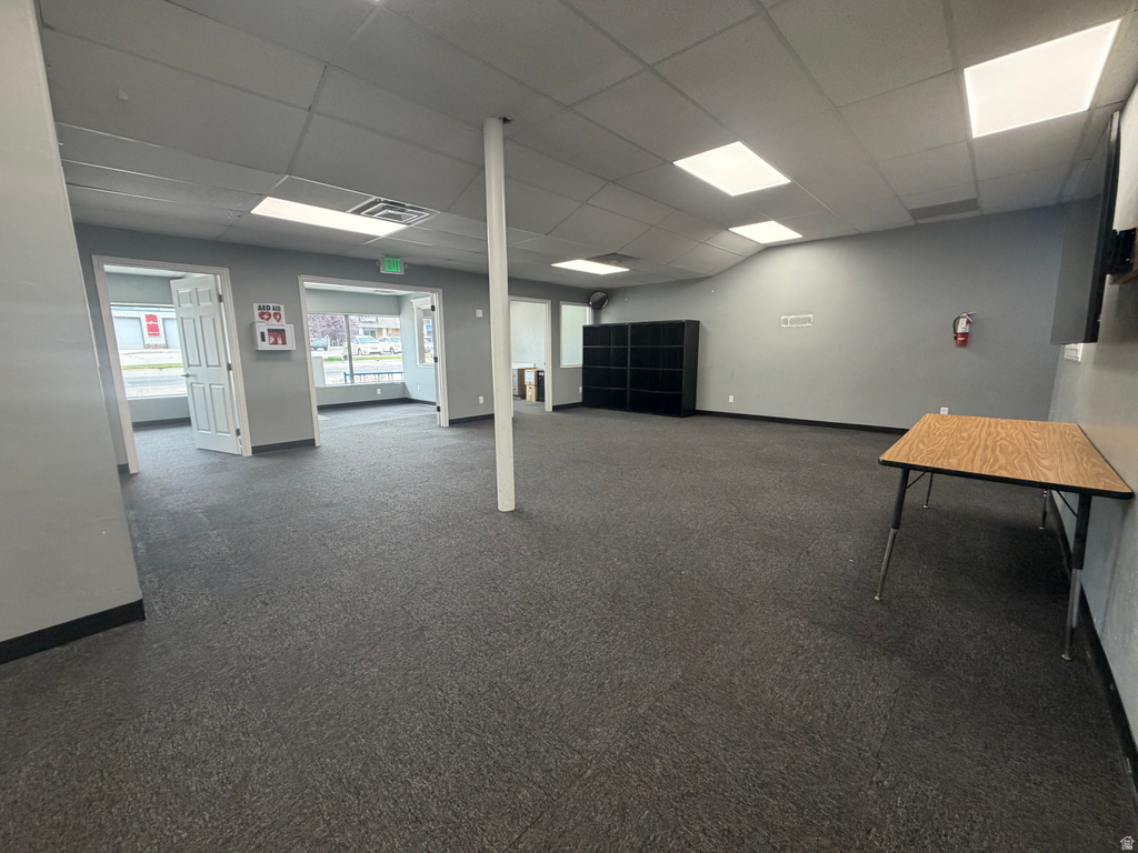 Spacious interior featuring grey carpeting, drop ceiling with recessed lighting, multiple windows, and light grey walls