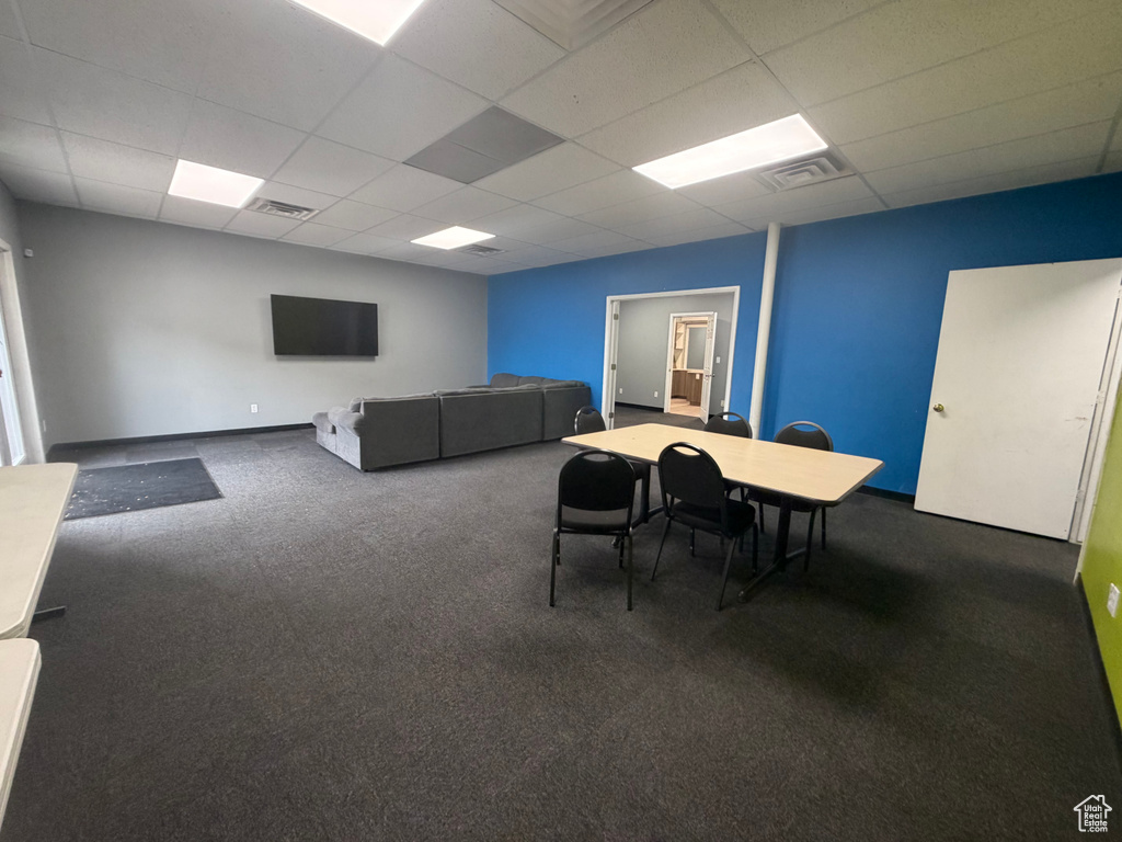 Spacious room featuring dark gray carpeting, a mix of blue and gray wall paint, and white ceiling tiles with recessed lighting