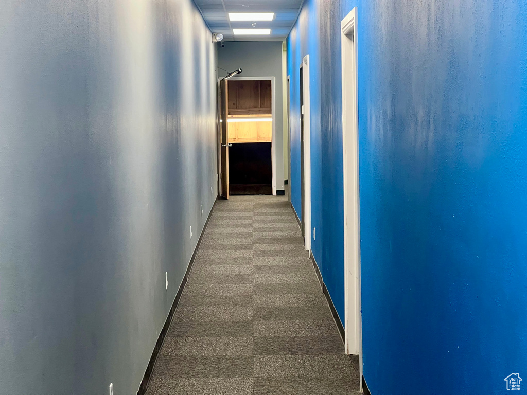 Hallway featuring baseboards and dark carpet