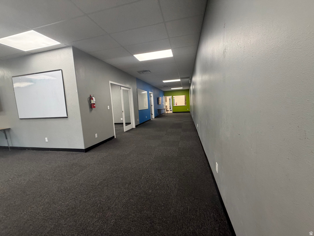 Spacious interior corridor with dark gray carpeting, light gray walls, and recessed fluorescent lighting