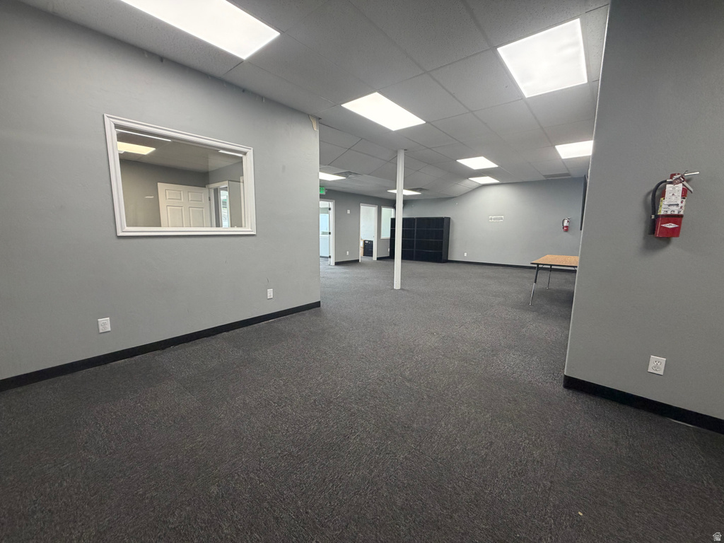 Open-concept commercial interior featuring gray walls, dark patterned carpet, and a drop ceiling with integrated rectangular lighting