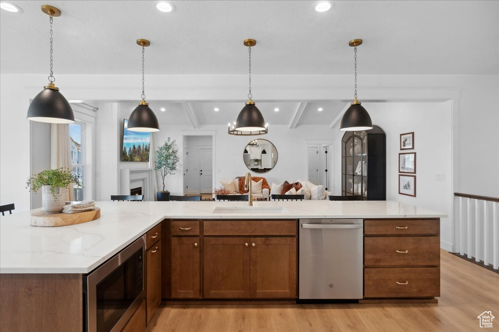 Kitchen featuring appliances with stainless steel finishes, hanging light fixtures, light wood-type flooring, light stone countertops, and recessed lighting