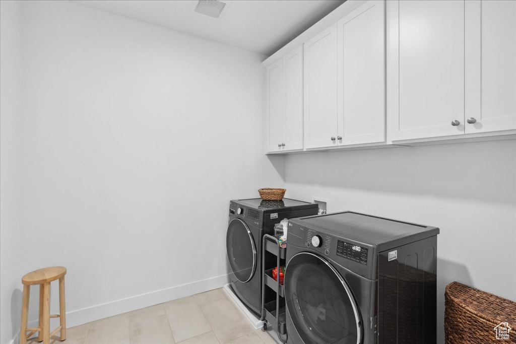Laundry area with cabinet space, washing machine and dryer, and light tile patterned flooring