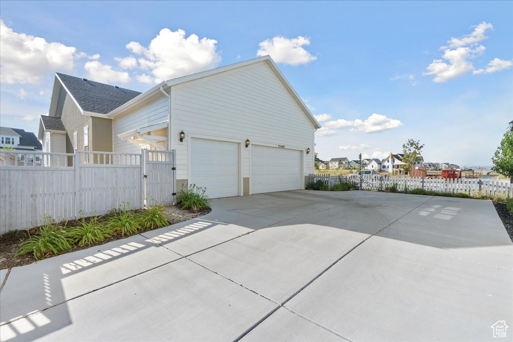 View of side of home featuring concrete driveway, a residential view, a shingled roof, and a garage