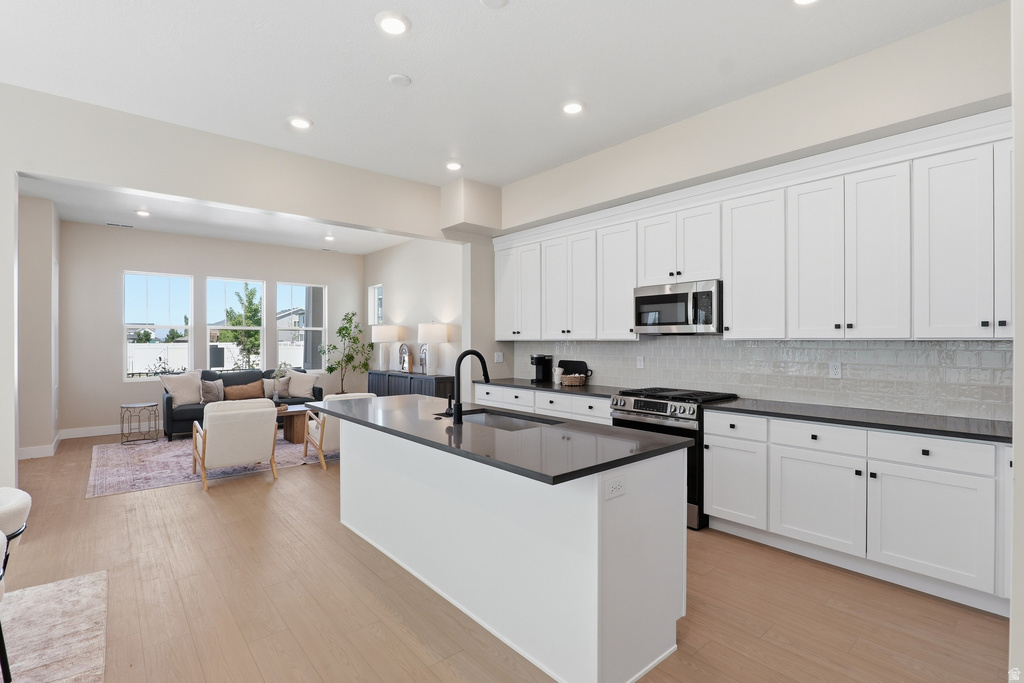 Open-concept kitchen and living area featuring white cabinetry, dark countertops, stainless steel appliances, and light wood-finish flooring