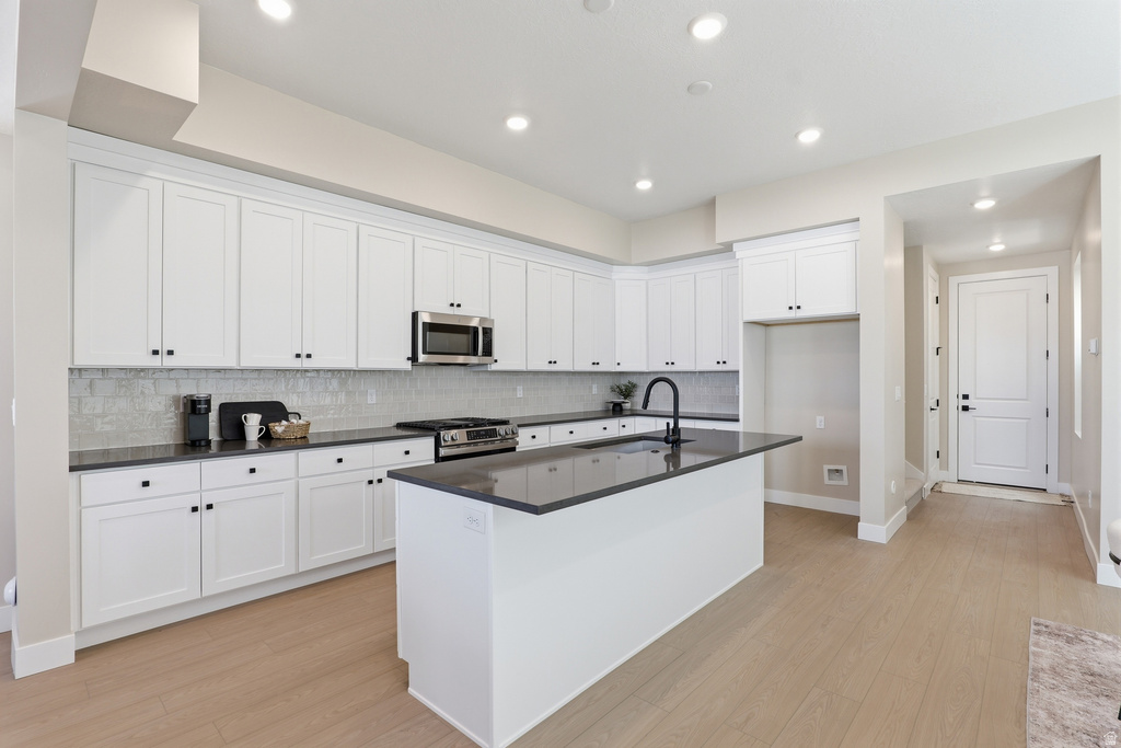 Modern kitchen featuring extensive white cabinetry, dark countertops, a stainless steel microwave, a center island with a black faucet, and light wood-finish flooring
