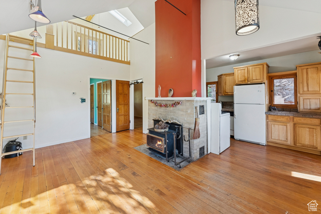 Unfurnished living room featuring high vaulted ceiling, light wood finished floors, a skylight, and a wood stove