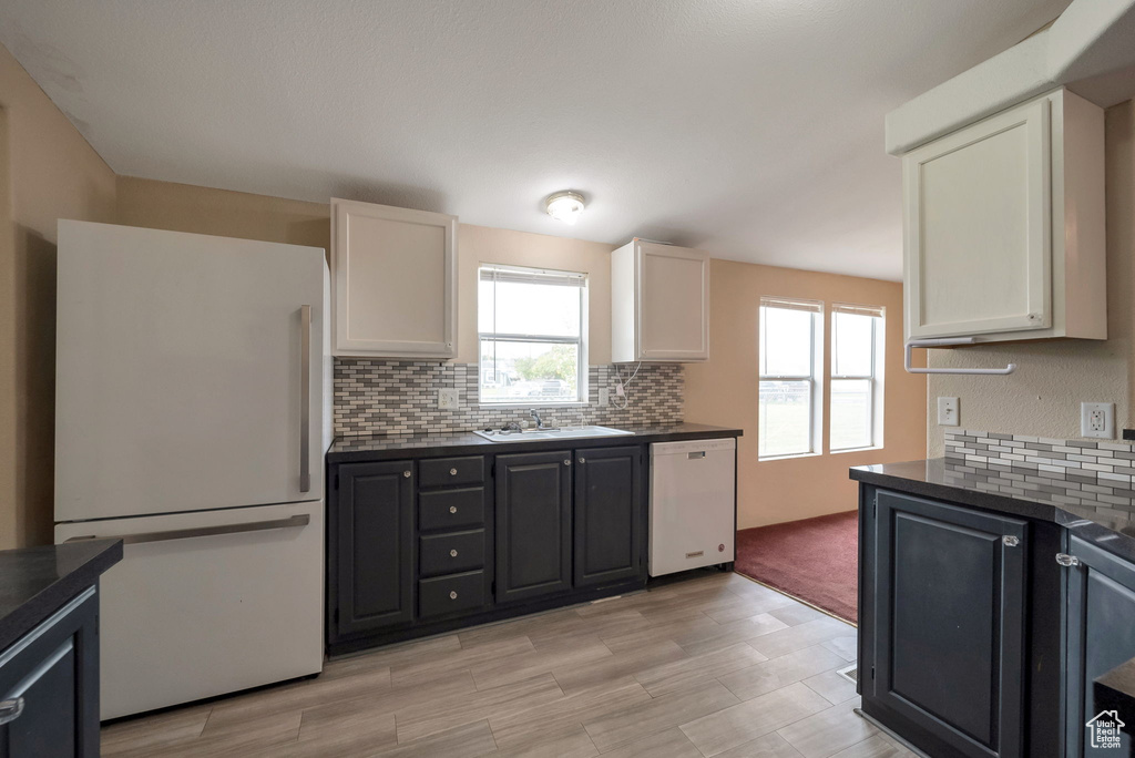Kitchen featuring white appliances, decorative backsplash, light wood finished floors, dark cabinets, and white cabinets