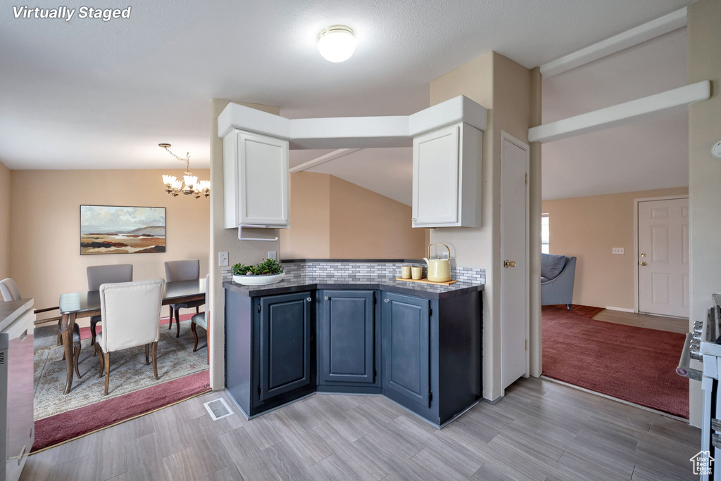 Kitchen with white cabinets, a chandelier, tasteful backsplash, stainless steel gas range, and lofted ceiling