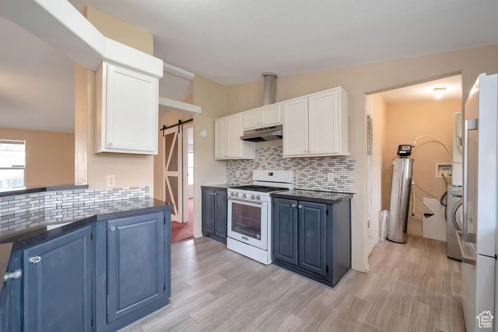 Kitchen featuring a barn door, white cabinets, decorative backsplash, white appliances, and vaulted ceiling