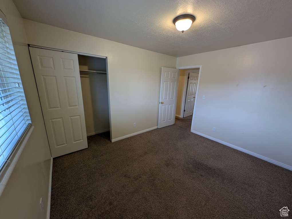 Unfurnished bedroom featuring dark colored carpet, a textured ceiling, and a closet