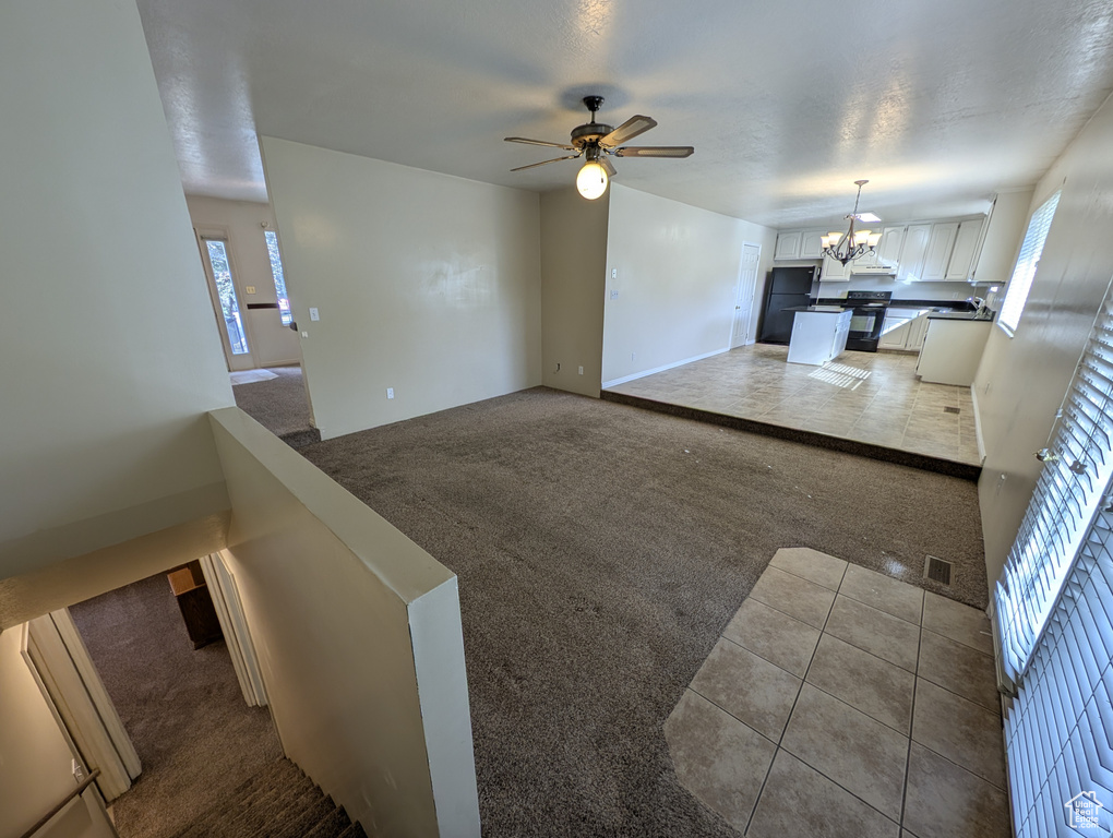 Unfurnished living room with dark colored carpet, dark tile patterned floors, ceiling fan, and a chandelier