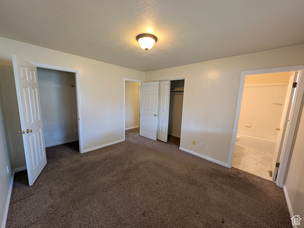Unfurnished bedroom with carpet floors, a textured ceiling, multiple closets, and ensuite bath
