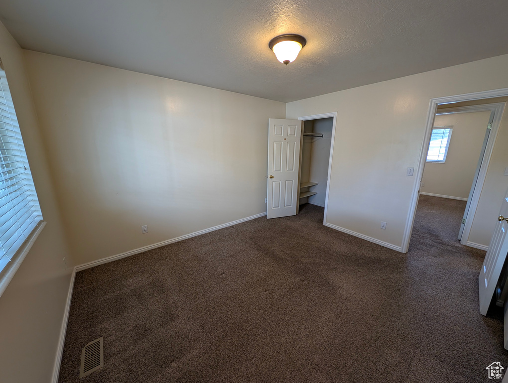 Unfurnished bedroom with carpet, a textured ceiling, and a spacious closet