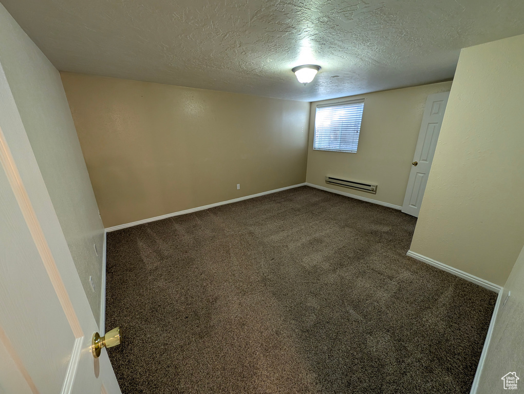 Empty room with carpet, a textured ceiling, and baseboard heating