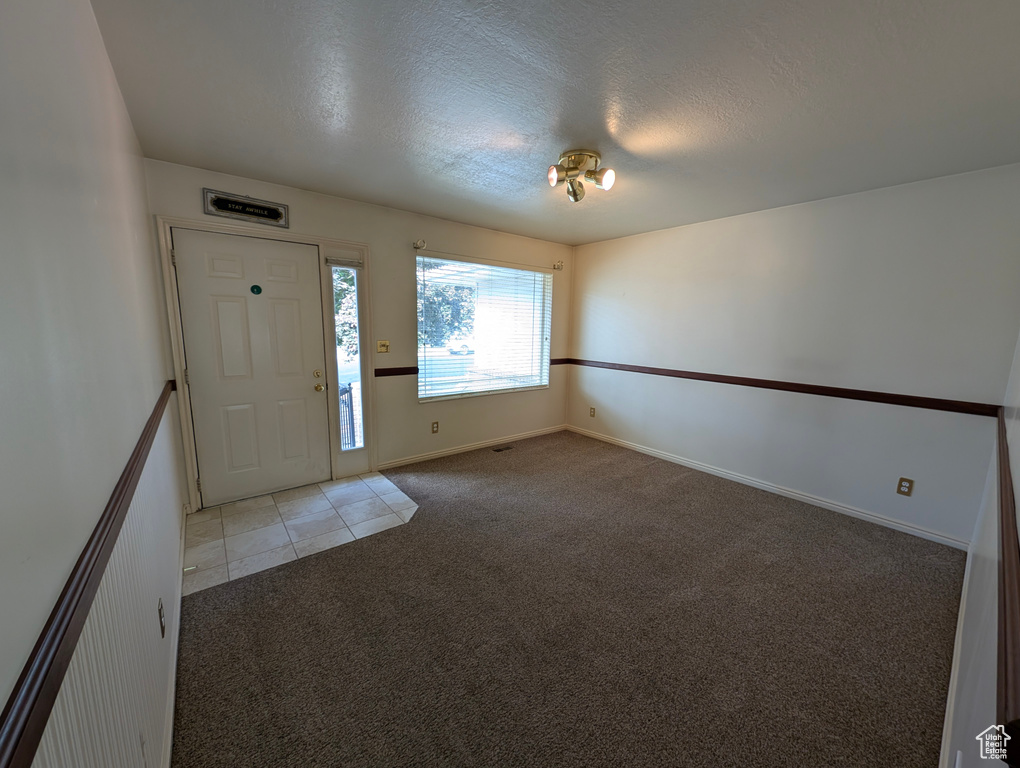 Entrance foyer with light colored carpet, a textured ceiling, and light tile patterned floors