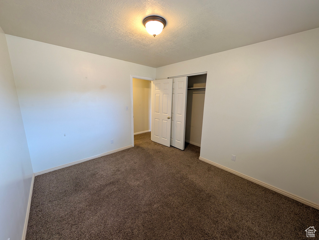 Unfurnished bedroom featuring a textured ceiling, dark colored carpet, and a closet