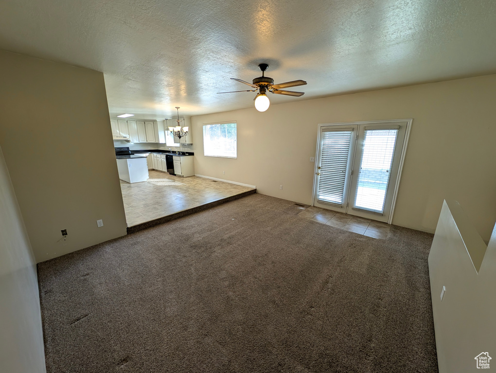 Unfurnished living room featuring a textured ceiling, light carpet, a ceiling fan, a chandelier, and light tile patterned flooring