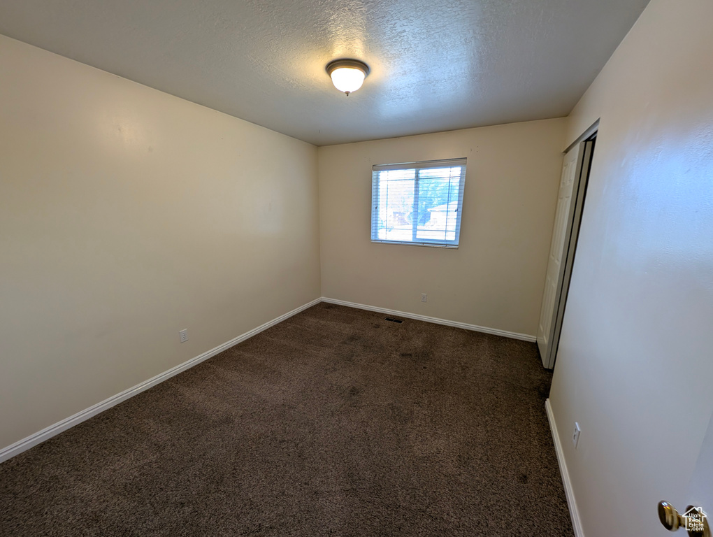 Spare room with dark carpet and a textured ceiling