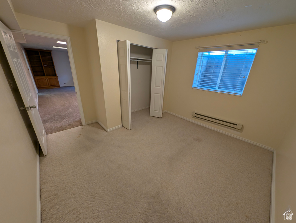 Unfurnished bedroom featuring carpet flooring, a textured ceiling, a baseboard heating unit, and a closet